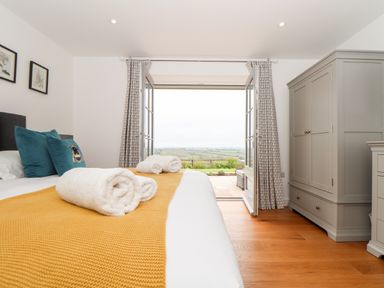 A bedroom with a bed with towels and pillows facing open doors with a view outside at Trevilges Cottage Trewennack near Helston