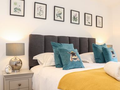 A bedroom with a bed headboard pillows lamps and framed botanical prints at Trevilges Cottage Trewennack near Helston