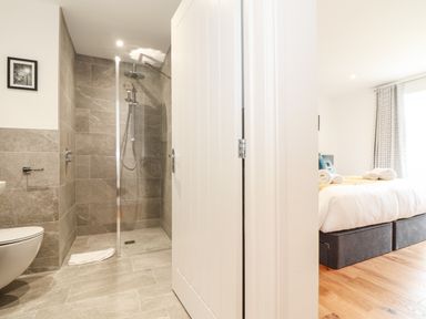 A bathroom with a walk-in shower and a view of a bedroom with a bed and window at Trevilges Cottage Trewennack near Helston