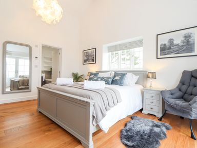 A bedroom with a bed gray blanket pillows a gray nightstand lamp a gray chair and a full length mirror at Trevilges Cottage Trewennack near Helston