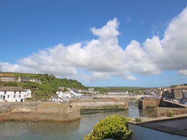 A view of a harbor with stone piers and buildings on the shore under a blue sky with clouds at Trevilges Cottage Trewennack near Helston