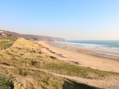 A sandy beach with waves and grassy cliffs overlooking the ocean near Trevilges Cottage Trewennack near Helston