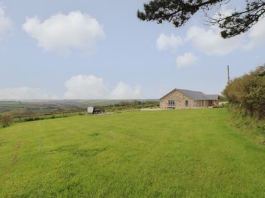 A stone house with a large grassy lawn and countryside view at Trevilges Cottage in Trewennack near Helston