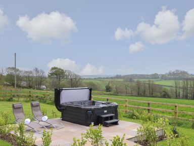 An outdoor patio with a hot tub and two lounge chairs with towels on a grassy field at Trevilges Cottage Trewennack near Helston