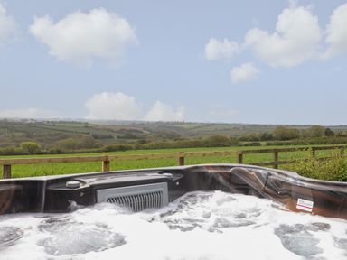 An outdoor hot tub with bubbles and a view of green fields and hills at Trevilges Cottage Trewennack near Helston