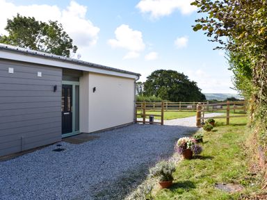 A house entrance with a gravel driveway and a wooden fence with flower pots along the side at The Linhay in Lapford