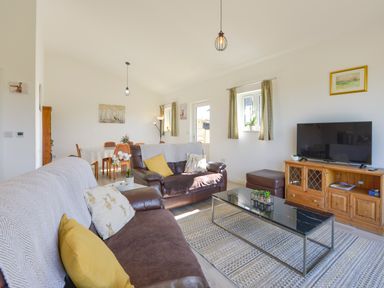 A living room with brown leather sofas a glass coffee table a wooden TV stand and a dining table at The Linhay in Lapford