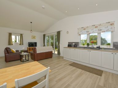 An open plan kitchen and living room with brown sofas a wooden dining table and white cabinets at The Linhay in Lapford