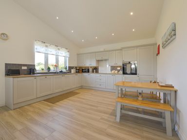 A kitchen with gray cabinets wooden countertop dining table and bench with chairs at The Linhay in Lapford