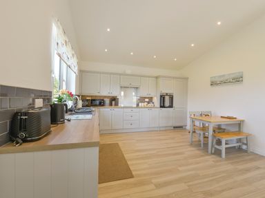 A kitchen with wooden countertops grey cabinets a dining table and chairs and a bench at The Linhay in Lapford