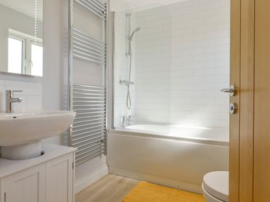 A bathroom with a sink cabinet towel heater bathtub with shower screen and a yellow mat at The Linhay in Lapford