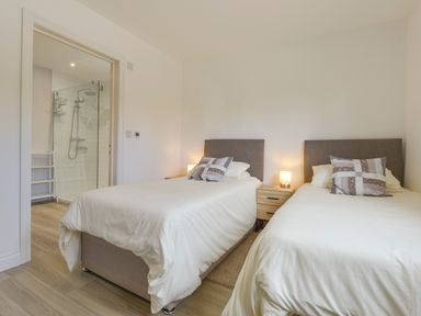 A bedroom with two single beds a nightstand with lamps and an en suite bathroom at The Linhay in Lapford