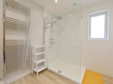 A bathroom with a walk in shower a metal towel rack a white storage shelf and a window at The Linhay in Lapford