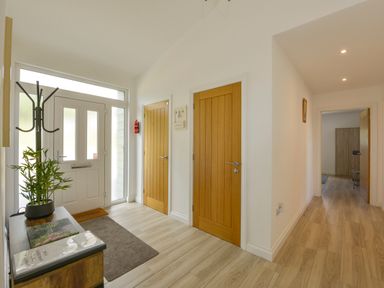An entrance hallway with wooden doors a white front door a plant on a cabinet and a long corridor at The Linhay in Lapford