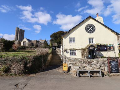 A stone church and a building with a sign for The Carpenters Arms with benches outside at The Old Chapel in Ilsington