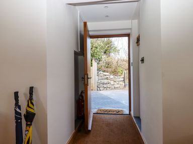 An entry hallway with two umbrellas and an open wooden door showing a stone wall outside at The Old Chapel in Ilsington