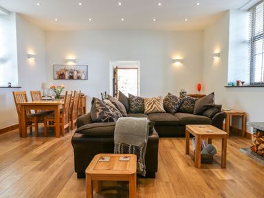 A living room with a dark sofa and wooden tables next to a dining table with six chairs at The Old Chapel in Ilsington
