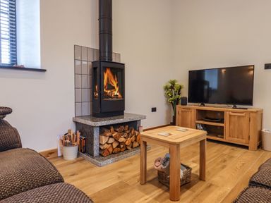 A living room with a wood burning stove TV on a wooden cabinet wooden coffee table and sofas at The Old Chapel in Ilsington