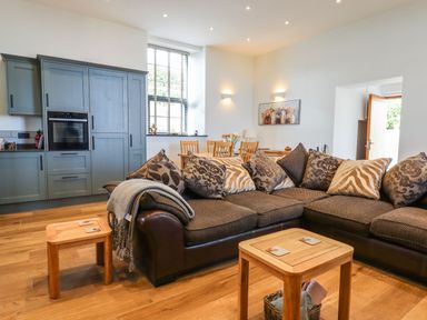 An open living room and kitchen with a sectional sofa and dining table at The Old Chapel in Ilsington