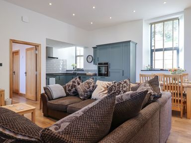 An open plan living area with a sofa and cushions a dining table with chairs and a kitchen with cabinets and appliances at The Old Chapel in Ilsington