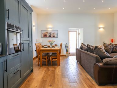 A dining area with wooden table and chairs next to a living room with a sofa and cushions at The Old Chapel in Ilsington