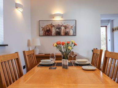 A dining room with a wooden table and chairs flowers in a vase and a painting of three cows on the wall at The Old Chapel in Ilsington