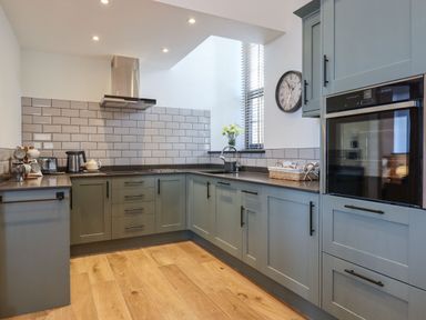 A kitchen with gray cabinets wooden floor and a window with blinds at The Old Chapel in Ilsington