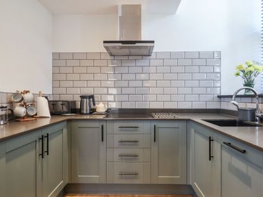A kitchen with light gray cabinets a stainless steel range hood a toaster kettle and flowers in a vase at The Old Chapel in Ilsington