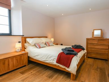 A bedroom with a wooden bed a lamp on a side table and a wooden dresser at The Old Chapel in Ilsington