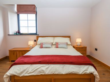 A bedroom with a wooden bed frame white bedding red throw and two bedside tables with lamps at The Old Chapel in Ilsington