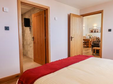 A bedroom with a bed and red blanket and two open doors showing a bathroom and a dining room at The Old Chapel in Ilsington