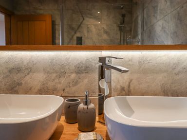 A bathroom counter with two white sinks a soap dispenser and a cup with a mirror and wooden door in the background at The Old Chapel in Ilsington