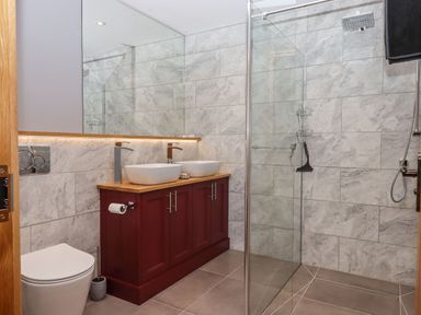 A bathroom with a toilet double sinks a wooden vanity and a glass shower at The Old Chapel in Ilsington