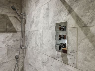 A shower area with a handheld showerhead and control knobs on tiled walls at The Old Chapel in Ilsington