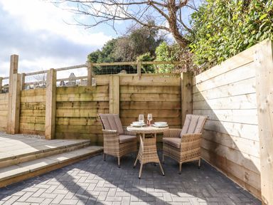 A small outdoor seating area with a round table and two wicker chairs with cushions at The Old Chapel in Ilsington