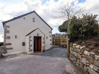 Exterior of a white building with stone accents and wooden door next to stone wall and outdoor seating at The Old Chapel in Ilsington