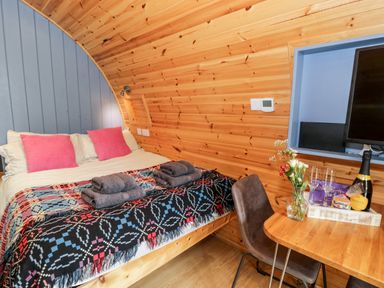 A bedroom with a double bed with folded towels and a table with flowers glasses and a bottle at Conwy Pod in Capel Garmon near Betws Y Coed