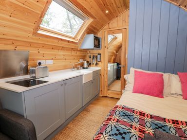 A small kitchen area with blue cabinets and a toaster next to a bed with pink pillows and a patterned blanket at Conwy Pod in Capel Garmon near Betws-Y-Coed