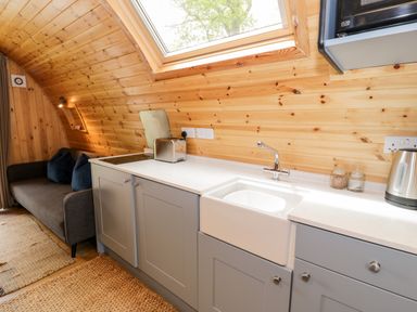 A kitchen area with gray cabinets sink toaster and a kettle next to a seating area with a sofa and pillows at Conwy Pod in Capel Garmon near Betws-Y-Coed