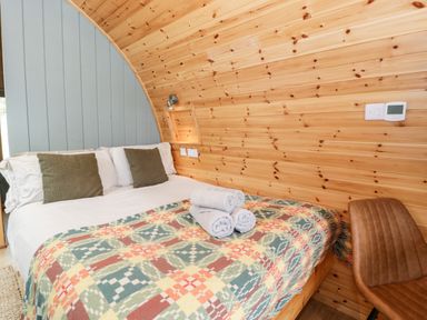 A bed with folded towels and pillows in a wooden pod room with a brown chair at Llugwy Pod in Capel Garmon near Betws-Y-Coed