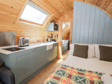 A compact kitchen area with cabinets microwave toaster and sink next to a bed with pillows and a patterned blanket at Llugwy Pod in Capel Garmon near Betws-Y-Coed