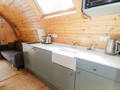 A kitchen area with cabinets a sink a toaster a kettle and a sofa beside it at Llugwy Pod in Capel Garmon near Betws-Y-Coed