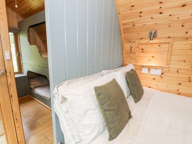 A bedroom with a bed with white sheets and green pillows and built-in bunk beds with a window at Llugwy Pod in Capel Garmon near Betws-Y-Coed