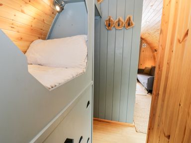A small bed with a pillow and light attached on a wooden wall next to a grey wall with wooden hooks and a grey sofa in a wooden room at Llugwy Pod in Capel Garmon near Betws-Y-Coed