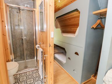 A bathroom with a toilet and shower next to a room with built-in bunk beds and a small closet with hangers at Llugwy Pod in Capel Garmon near Betws-Y-Coed
