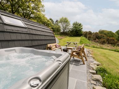 An outdoor area with a hot tub wooden benches a picnic table and trees at Llugwy Pod in Capel Garmon near Betws-Y-Coed