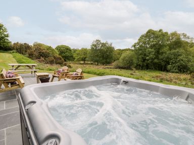 An outdoor hot tub with bubbling water near wooden chairs and a picnic table in a grassy area at Llugwy Pod in Capel Garmon near Betws-Y-Coed
