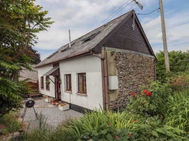 Exterior of a small house with a stone and plaster wall and a garden with plants and flowers at Northwood Barn in Okehampton