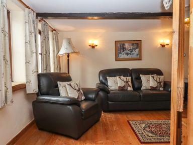 A living room with leather sofa and armchair with deer cushions a floor lamp curtains with deer pattern and a painting on the wall at Northwood Barn in Okehampton