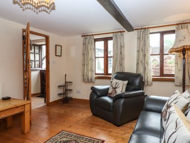 A living room with leather armchairs wooden floors curtains with deer patterns and a wooden coffee table at Northwood Barn in Okehampton